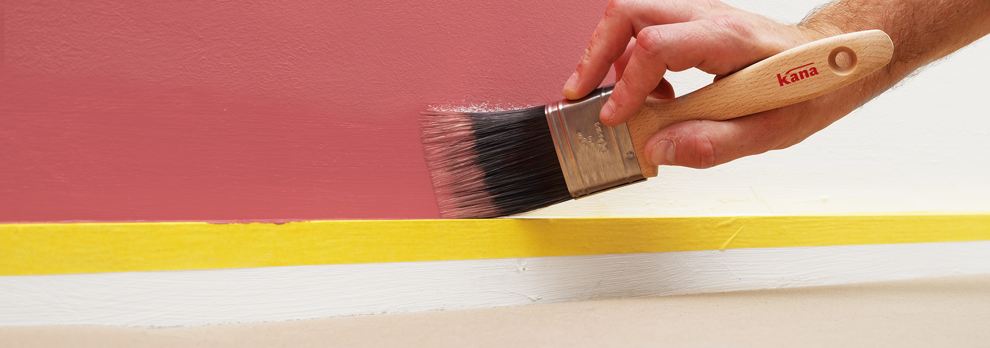 Kana paint brush is used to paint a smooth line on the wall above skirting board.